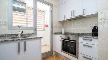 Una cocina con armarios blancos, un horno Bosch, una ventana con persianas y un salpicadero de azulejos.