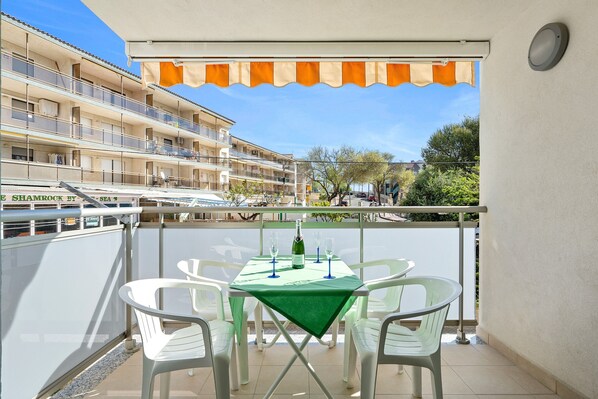 A balcony with a table and chairs, a view of a building, and a ship in the background.