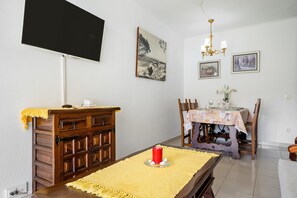 A dining area with a table set for four, a wooden cabinet, a TV mounted on the wall, and framed pictures on the wall.