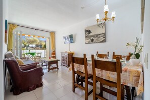 A dining area with a table set for four, a sofa, a television, and a painting on the wall.