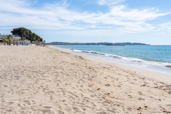 A sandy beach with footprints, a clear sky, and a distant shoreline with buildings.