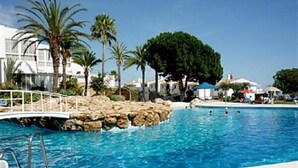 Une piscine à l’eau d’un bleu cristallin, entourée de palmiers et surplombée par un pont blanc.