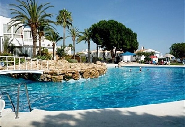 A pool with clear blue water, surrounded by palm trees and a white bridge.