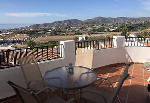 A terrace with a table and chairs, a view of a town and hills in the background.