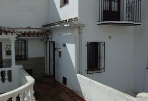 A narrow alleyway with a tiled floor, white walls, and a small door with a metal gate.