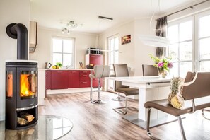 A modern kitchen with a wood-burning stove, a dining area with a table and chairs, and a red cabinet.