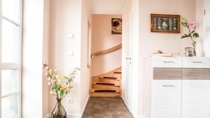 A hallway with a staircase, a white cabinet, and a vase with flowers. - House Rose, luxury vacation home in Fuhlendorf for 4 people with sauna and beach chair (Fuhlendorf)