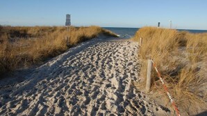 A sandy beach path with a signpost and a chain-link fence. - House Rose, luxury vacation home in Fuhlendorf for 4 people with sauna and beach chair (Fuhlendorf)