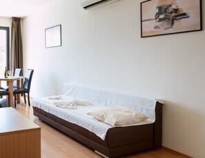 A modern, minimalist room with a brown sofa, a wooden table, and a chair. - Seaside Apartment with 2 Bedrooms for up to 5 Guests (Sunny Beach)