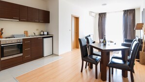 A modern kitchen with wooden cabinets, a dining table with chairs, and a view of the living area through a doorway. - Seaside Apartment with 2 Bedrooms for up to 5 Guests (Sunny Beach)