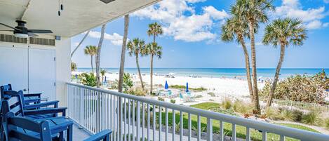 A balcony with chairs, a ceiling fan, and a view of the beach and ocean.