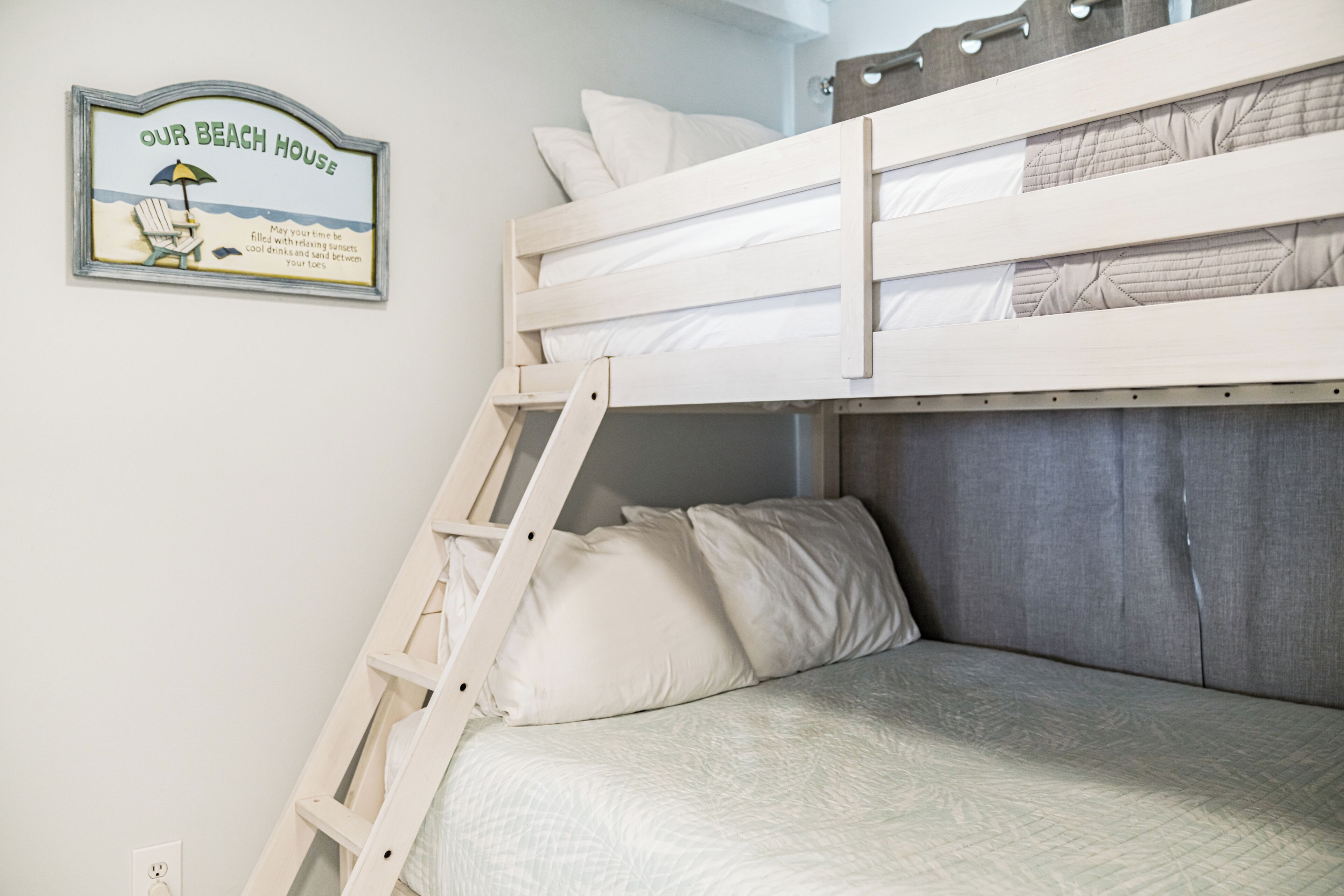 Un lit superposé avec une échelle, un oreiller et une pancarte fixée au mur sur laquelle on peut lire : « NOTRE MAISON DE VACANCES AU BORD DE LA MER ».
