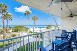 A balcony with a view of the beach, palm trees, and beach umbrellas.