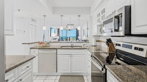 Cocina moderna con armarios blancos, encimeras de granito, horno empotrado y vistas al océano.