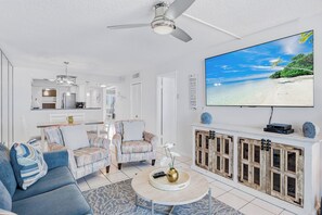 Una sala moderna con un televisor de pantalla plana, un ventilador de techo y vista a la playa.