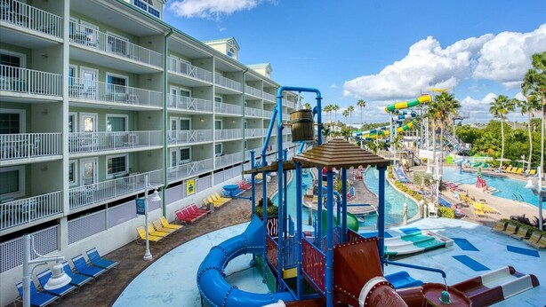 A hotel with multiple balconies, a water park area with slides and pools, and a clear blue sky.