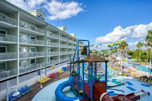 Un hotel con varios balcones, una zona de parque acuático con toboganes y piscinas, y un cielo azul despejado.