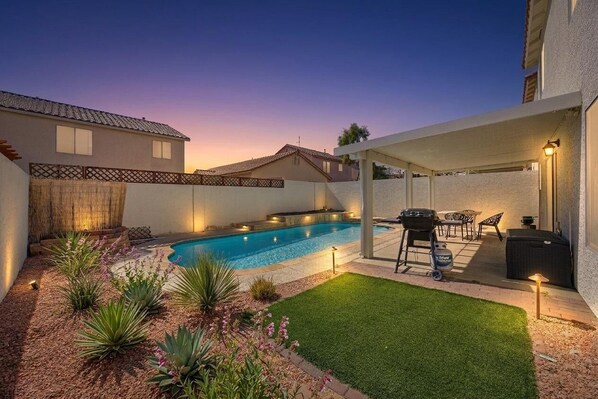 Un jardin avec une piscine, un espace barbecue et une terrasse couverte.
