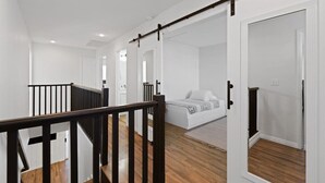 Um quarto espaçoso com piso de madeira, uma cama com cabeceira branca e corrimão preto.