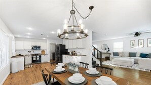 Cozinha moderna com armários brancos, área de refeições com mesa de madeira posta para quatro pessoas e escada que leva a uma sala de estar com sofá branco.