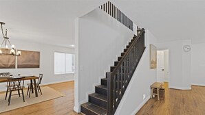 Um interior moderno com escada, piso de madeira e área de jantar com candelabro.