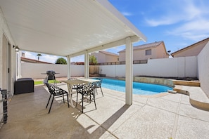 Un patio couvert avec une piscine, du mobilier d’extérieur et un barbecue.