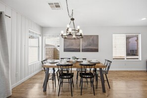 En spiseplads med et træbord dækket til seks personer, omgivet af sorte stole, under en moderne lysekrone.