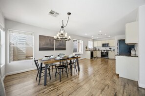 Une cuisine spacieuse avec un plancher en bois, un coin repas avec une table et des chaises en bois, et un lustre moderne.