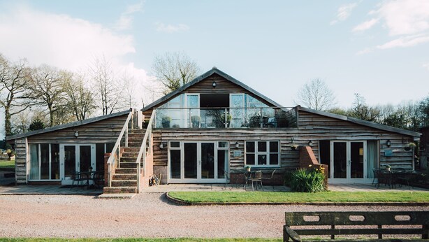 Une cabane en bois avec une extension en verre, un espace salon extérieur et une allée en gravier.