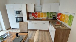 A modern kitchen with white cabinets, a microwave, oven, and a toaster. There is a dining table with a chair, a sink, and a window with a view of the outside.