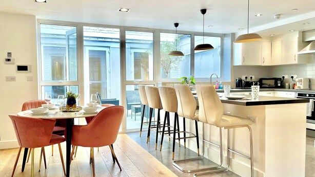 Una cocina moderna con una isla central, taburetes de bar y un comedor con mesa y sillas.