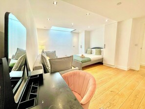 Una habitación moderna y bien iluminada con una cama, una zona de estar con mesa y sillas, y suelo de madera.