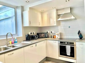 A modern kitchen with white cabinetry, a built-in oven, a microwave, and a coffee maker. - 3-bdr Holloway Flat W/ Patio near emirates stadium (Greater London)