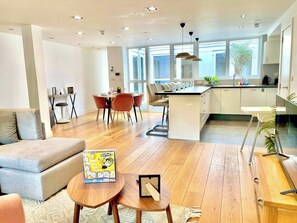 A modern kitchen with a dining area, wooden flooring, and large windows.