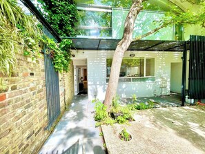 A narrow alleyway with a brick wall on one side and a metal gate on the other. There is a tree in the center of the alleyway. - 3-bdr Holloway Flat W/ Patio near emirates stadium (Greater London)