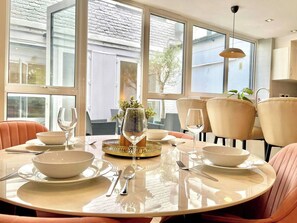 Un comedor con una mesa redonda preparada para dos personas, con platos, tazones y cubiertos blancos.