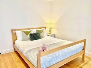 A single bed with a wooden frame, white bedding, and a green throw pillow. - 3-bdr Holloway Flat W/ Patio near emirates stadium (Greater London)