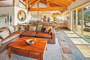 A spacious living room with a large brown leather sofa, a wooden coffee table, and a dining area with wooden chairs.