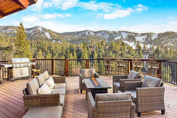 A deck with outdoor furniture, a grill, and a view of a mountainous landscape.