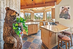 A kitchen with a bear sculpture, wooden cabinets, a large island, and a view of mountains.