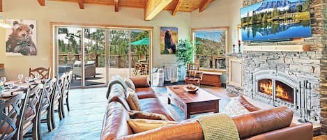 Amplia sala de estar con chimenea de piedra, sofá de cuero y zona de comedor con mobiliario exterior.