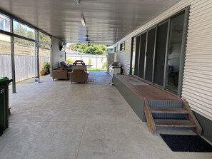 A covered patio area with outdoor furniture, a small table, and a trash bin.