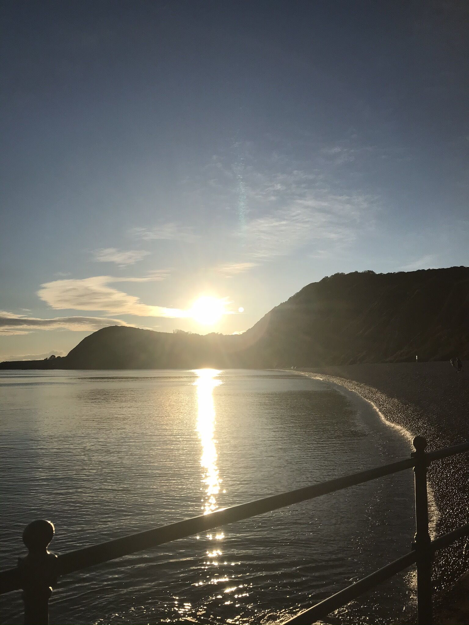 Un coucher de soleil sur une plage paisible, avec une rambarde en bois au premier plan.