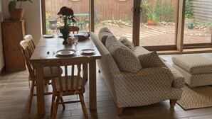 Un coin repas avec une table et des chaises en bois, un canapé et une vue sur le jardin à travers des portes vitrées.