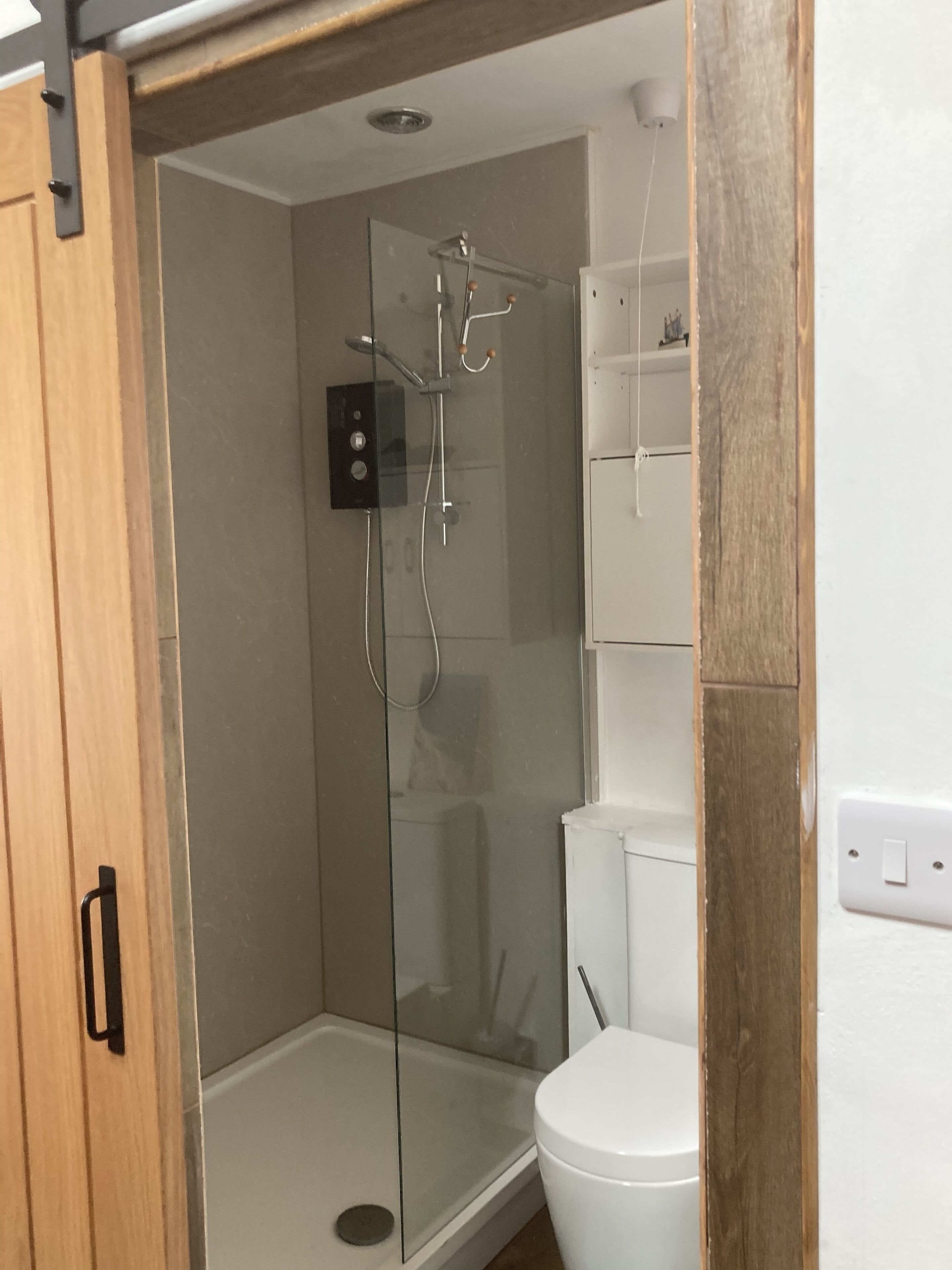 A compact bathroom with a glass shower enclosure, a white toilet, and a wooden door.