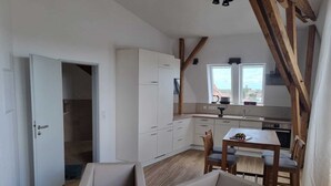 Een moderne keuken met witte kastjes, een eethoek met een tafel en stoelen, en uitzicht door de ramen.