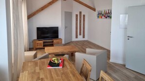 Een moderne woonkamer met een houten plafond, een flatscreen televisie, een eettafel met stoelen en een witte deur.