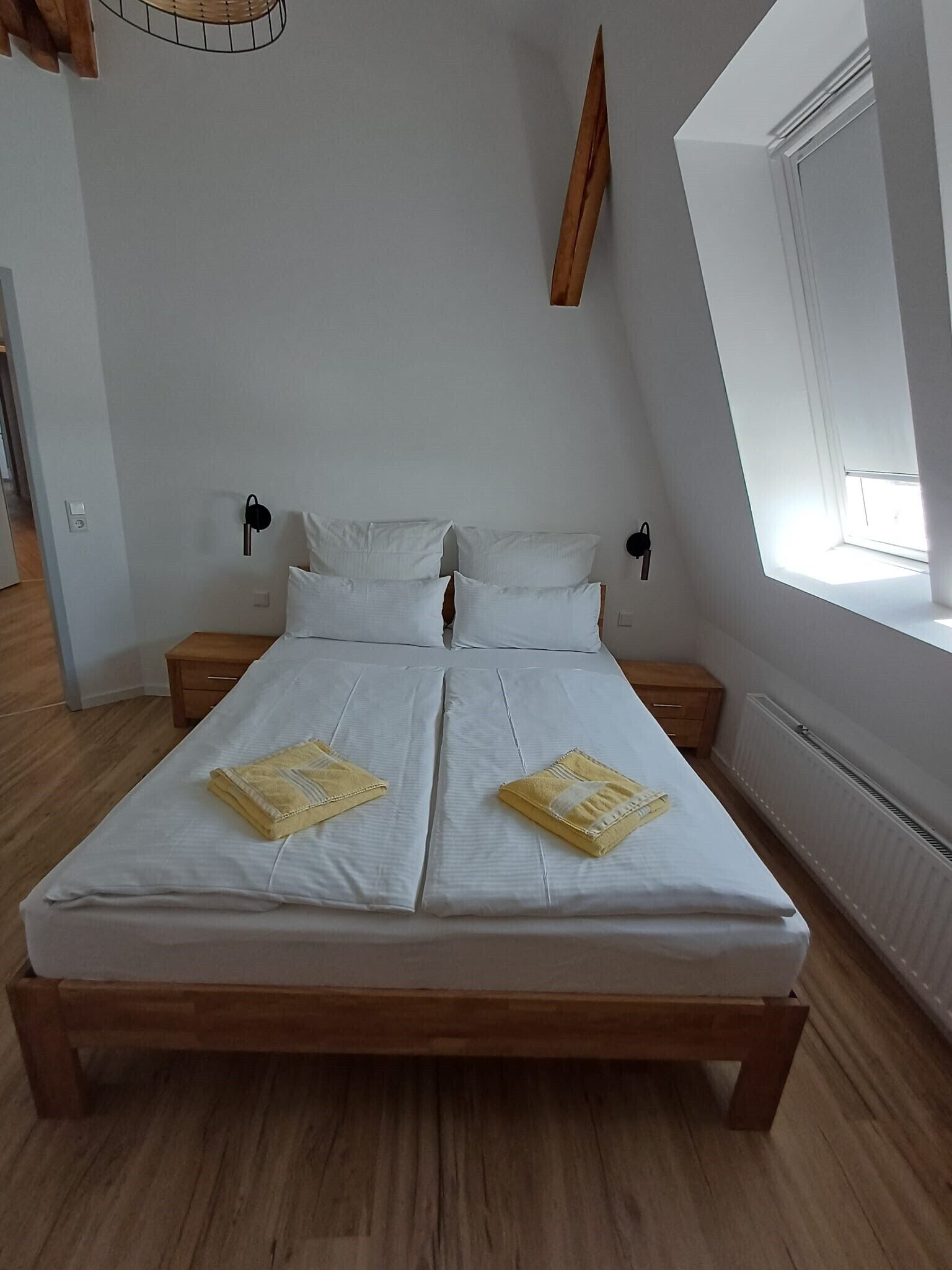 A bedroom with a large bed, two bedside tables, a window, and a wall-mounted light fixture.