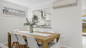 A dining area with a wooden table, white chairs, and a vase with greenery. - Coastal Soul - Belle Escapes Jervis Bay (Sanctuary Point)