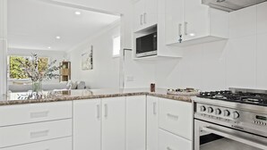 A modern kitchen with white cabinetry, a gas stove, and a built-in oven. - Coastal Soul - Belle Escapes Jervis Bay (Sanctuary Point)